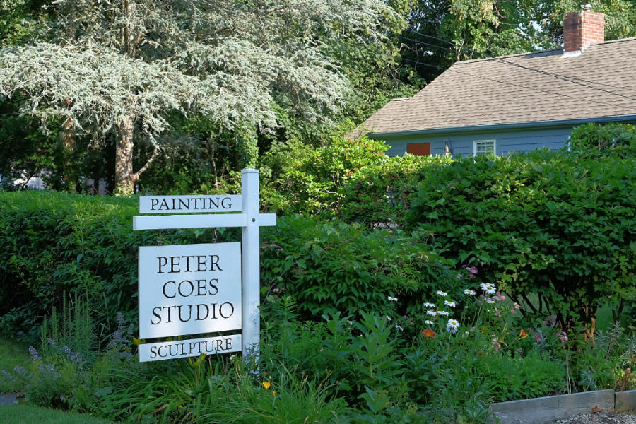 White sign in front of plantings and building